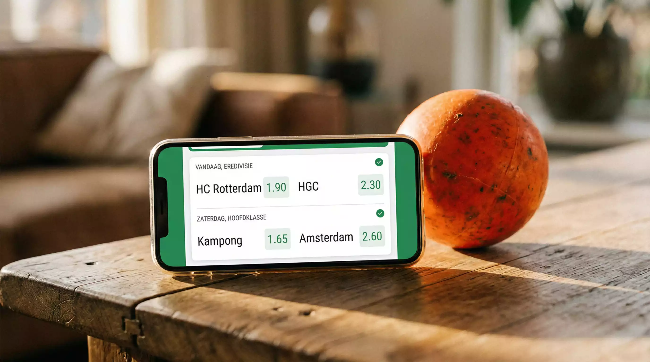 Smartphone met TOTO sportweddenschap app naast een oranje hockeybal