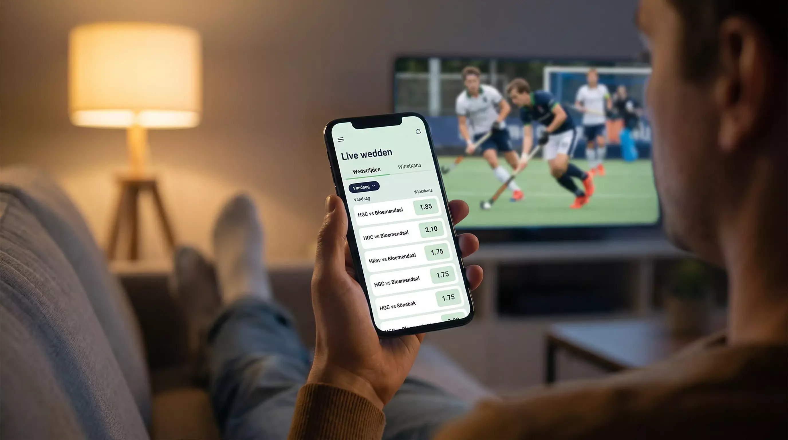Persoon gebruikt sportweddenschap app op smartphone met hockeywedstrijd op achtergrond